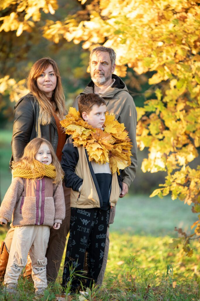 A family of four posing with autumn leaves, showcasing cozy fall fashion outdoors.