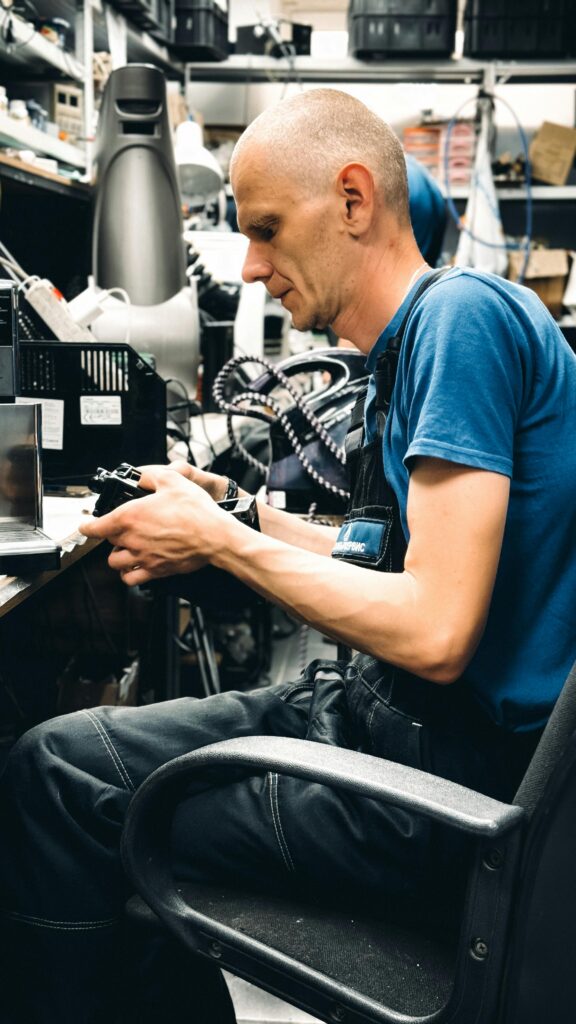Adult male technician repairing electronic devices in a cluttered workshop setting.