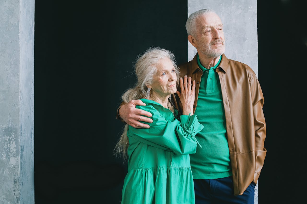 An elderly couple standing and embracing, clad in earthy tones, conveying love and togetherness.